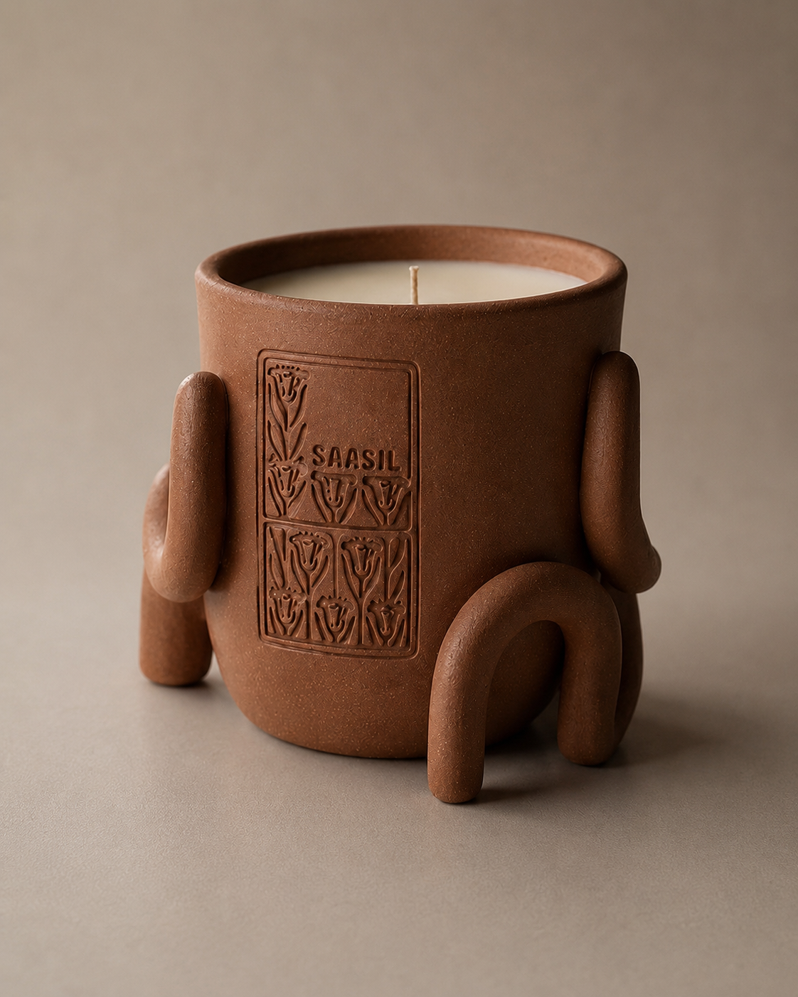 Saasil ceramic candle vessel in the Copal terracotta colorway, showing its sculptural looped base and debossed heritage mark